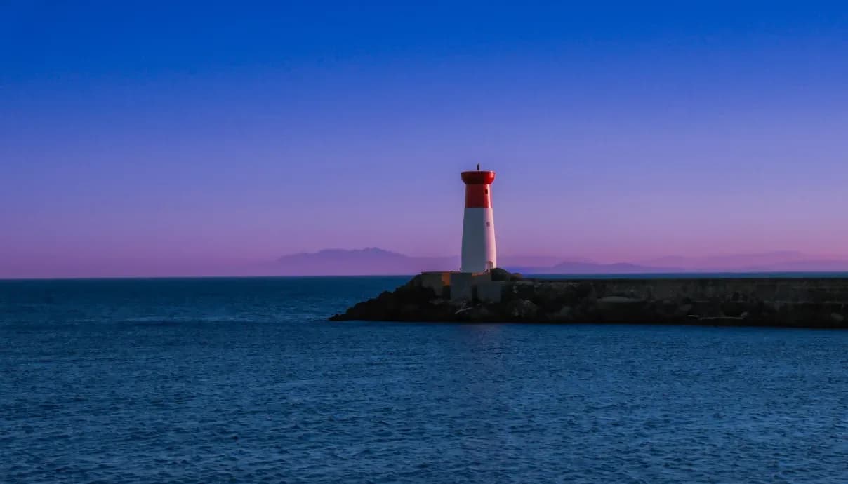 Phare rouge et blanc sur sa jetée au crépuscule, mer d'encre